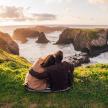 a couple sitting on a hill looking at the ocean