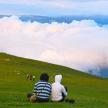two people sitting on a grassy hill looking at the clouds