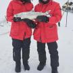 two people standing in the snow holding a fish
