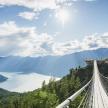 a suspension bridge in the mountains with a view of a lake