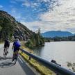 two people riding bikes on a road next to a lake