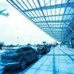 an airplane is flying over cars parked at an airport