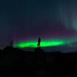 a person standing on a hill under the northern lights