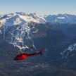 a red helicopter flying over a snow covered mountain
