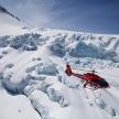 a red helicopter is flying over a snowy mountain