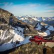 a red helicopter flying over a snowy mountain
