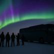 a group of people standing next to a bus under the northern lights