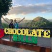 two women standing behind a sign that reads chocolate hills