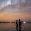 two people standing on the beach looking up at the universe