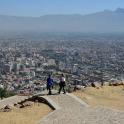 two people standing on top of a mountain looking at a city