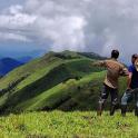 two men standing on top of a green mountain