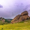 a large rock on a green field with a mountain