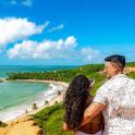 a man and woman standing on a cliff looking at a beach