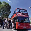 skupina lidí nastupujících do červeného dvoupatrového autobusu