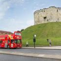 a red double decker bus driving past a castle