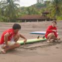 two young men sitting on a beach with surfboards