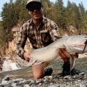 a man holding a large fish in front of a river