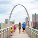 a group of people walking across a bridge with the gateway arch