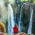a woman sitting on a rock in front of a waterfall