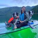a woman sitting on a paddle board with two dogs