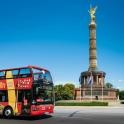 a red double decker bus driving past a statue
