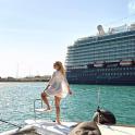 a woman standing on the back of a boat with a cruise ship