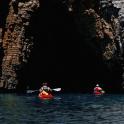 two people in kayaks in the water near a cave
