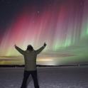 a man standing in the snow with his arms up under the northern lights