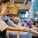 a man standing in a market with people holding cell phones