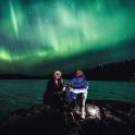 two people sitting on a rock under the northern lights