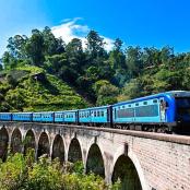 a blue train traveling on a bridge over a mountain