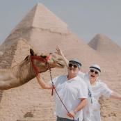 一名男子和一名女子站在金字塔旁的骆驼旁边