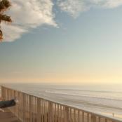 two people and a dog sitting on a fence at the beach