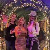 three women holding wine glasses in front of a barrel