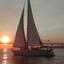 a sailboat in the water at sunset with a bridge