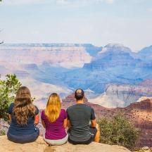 a group of people sitting on the edge of the grand canyon