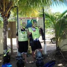 two men standing in front of a sign next to a palm tree