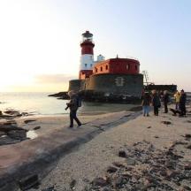 a group of people walking on the beach with a lighthouse