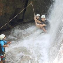 a group of three people rappelling down a waterfall