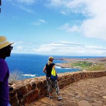 two people standing on a wall looking at the ocean