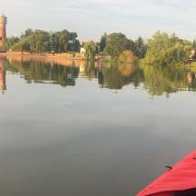 a red kayak on a river with trees and a tower