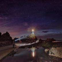 a person standing on a beach at night with a lighthouse