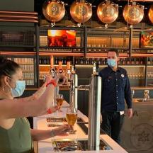 eine Frau mit Maske, die in einer Bar einen Drink zubereitet