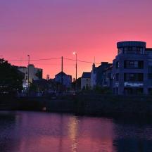 a sunset over a city with a river and buildings