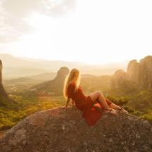 a woman sitting on a rock overlooking a valley