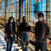 three people wearing masks standing in front of a stained glass wall