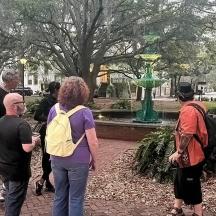 a group of people standing around a fountain in a park