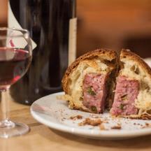 a sandwich on a plate next to a glass of wine