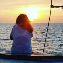 a woman sitting on a boat watching the sunset