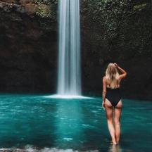 a woman standing in the water in front of a waterfall
